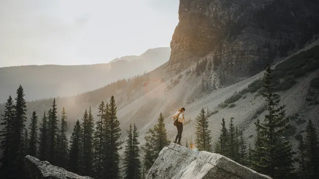 A hiker standing on a rock, looking out over mountains at sunset