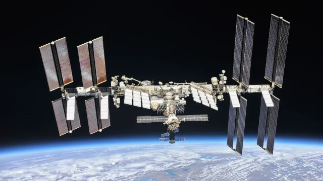 The whole International Space Station, with its long solar panels, above the blue edge of the Earth